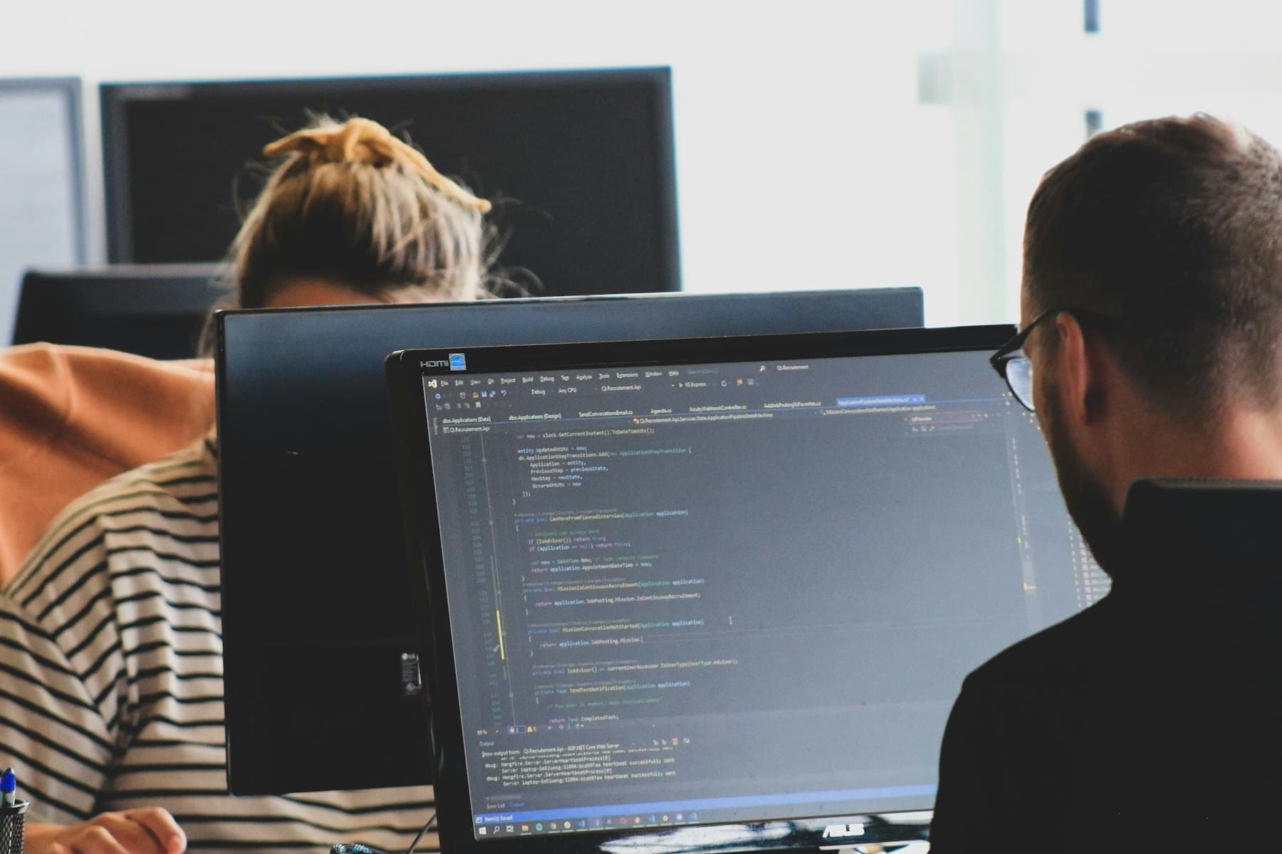Two people reviewing code on large monitors