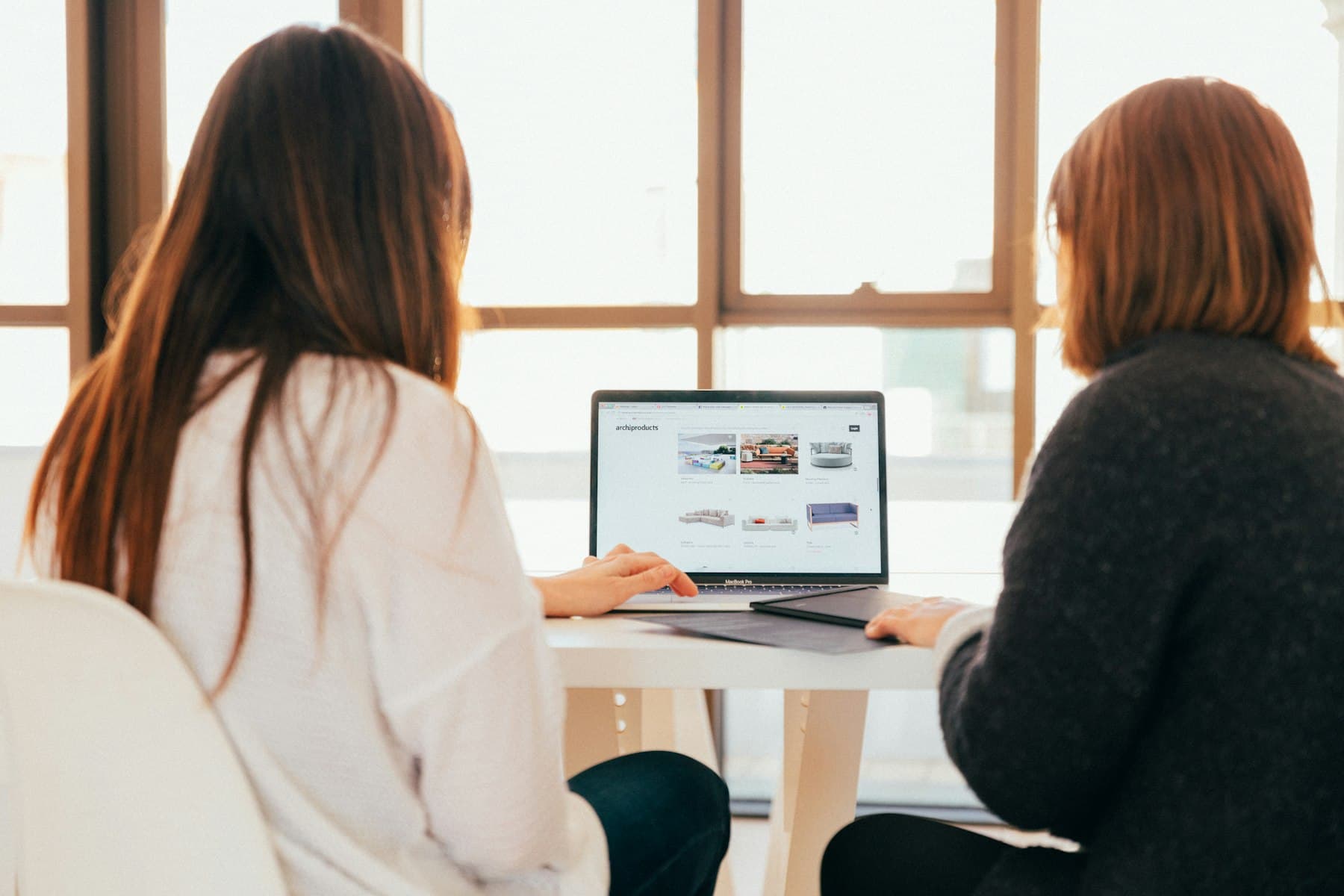 Two colleagues working together at a laptop by a window
